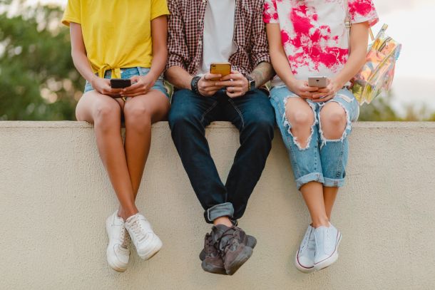 teenagers with their phones sit on a wall